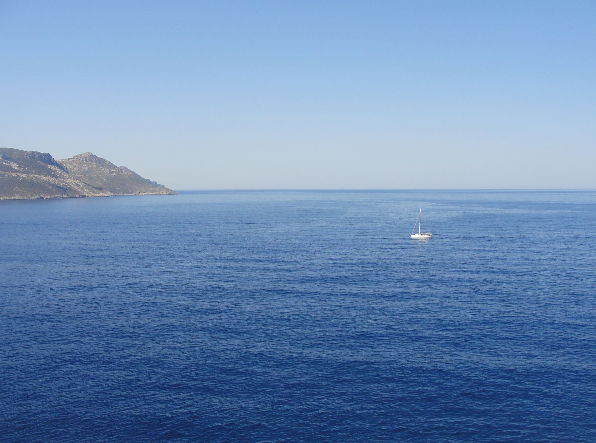 Minimal landscape with sail boat at calm sea and blue sky background. Sea with lonely white sail boat and coastline of greece island at the background                            